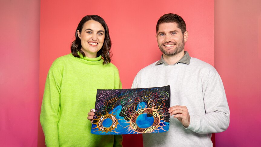 Woman and man smile for photo, man holds up artwork