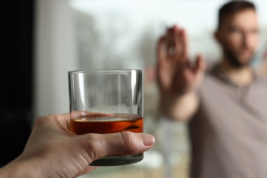 Blurred man in background refuses glass of whiskey 