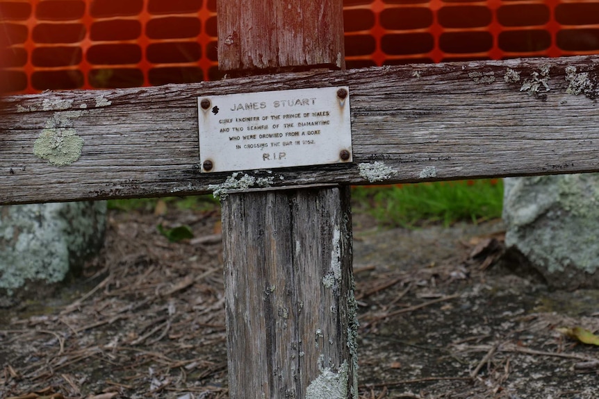 A close up of a plaque on a wooden cross, with the name 'James Stuart' and a small inscription.