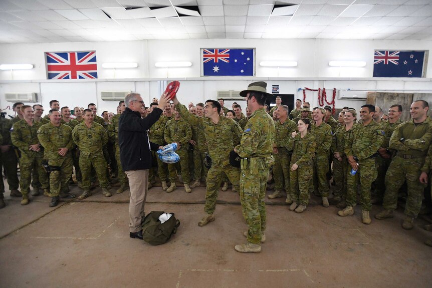 Mr Morrison is pictured surrounded by Australian troops, handing out footballs to the crowd and smiling.
