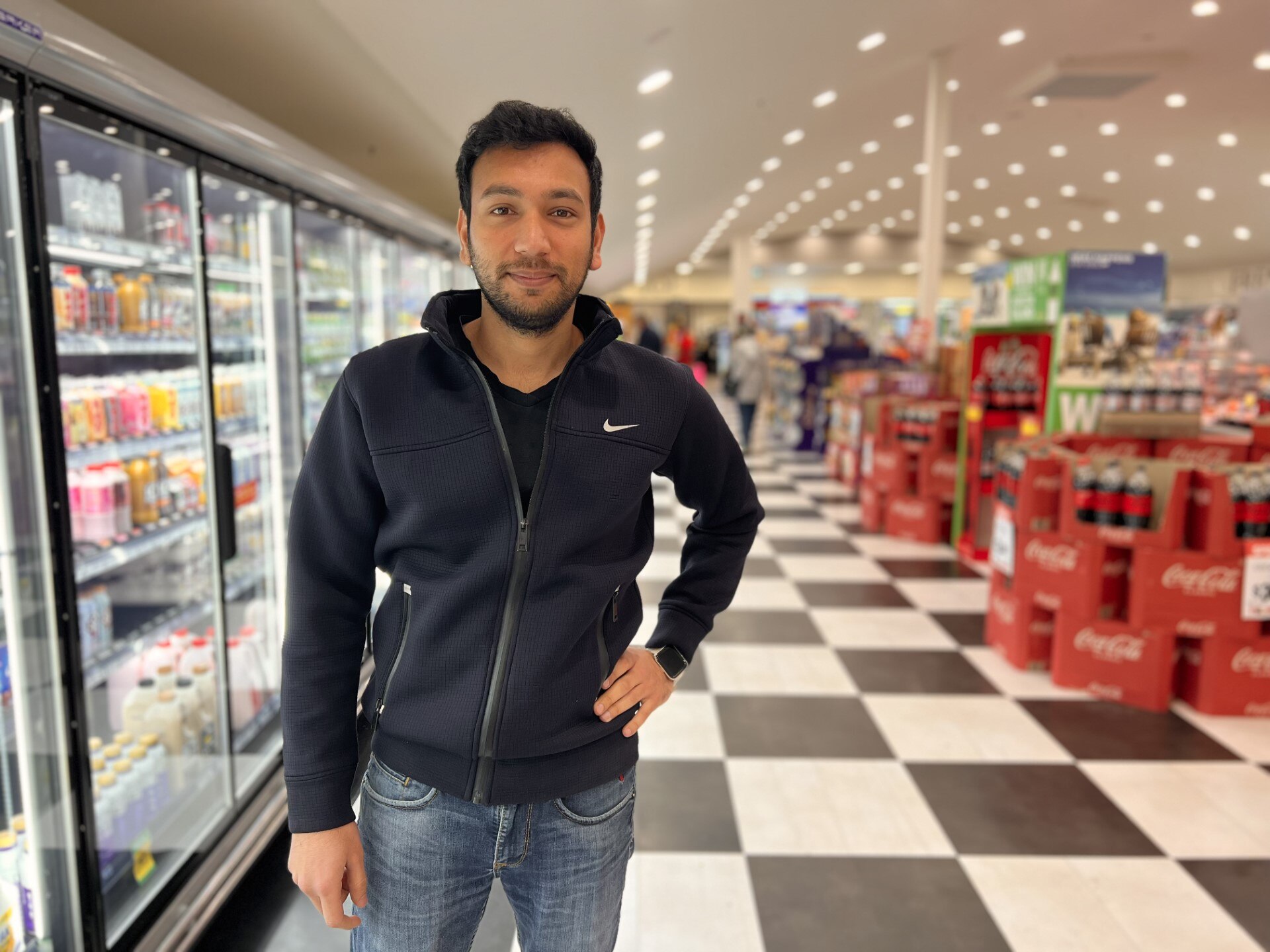 a dark haired olive skinned man stands in the middle of a supermarket aisle