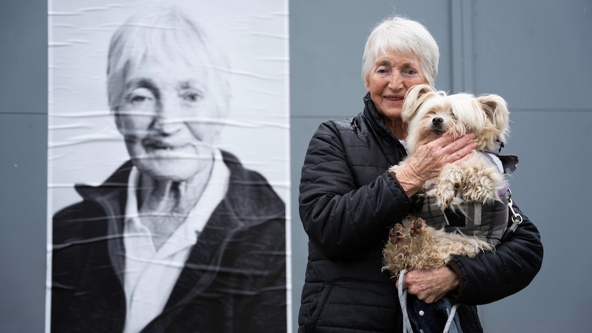 Di Harcourt with her dog Sammy, in front of a black and white photo portrait of herself.