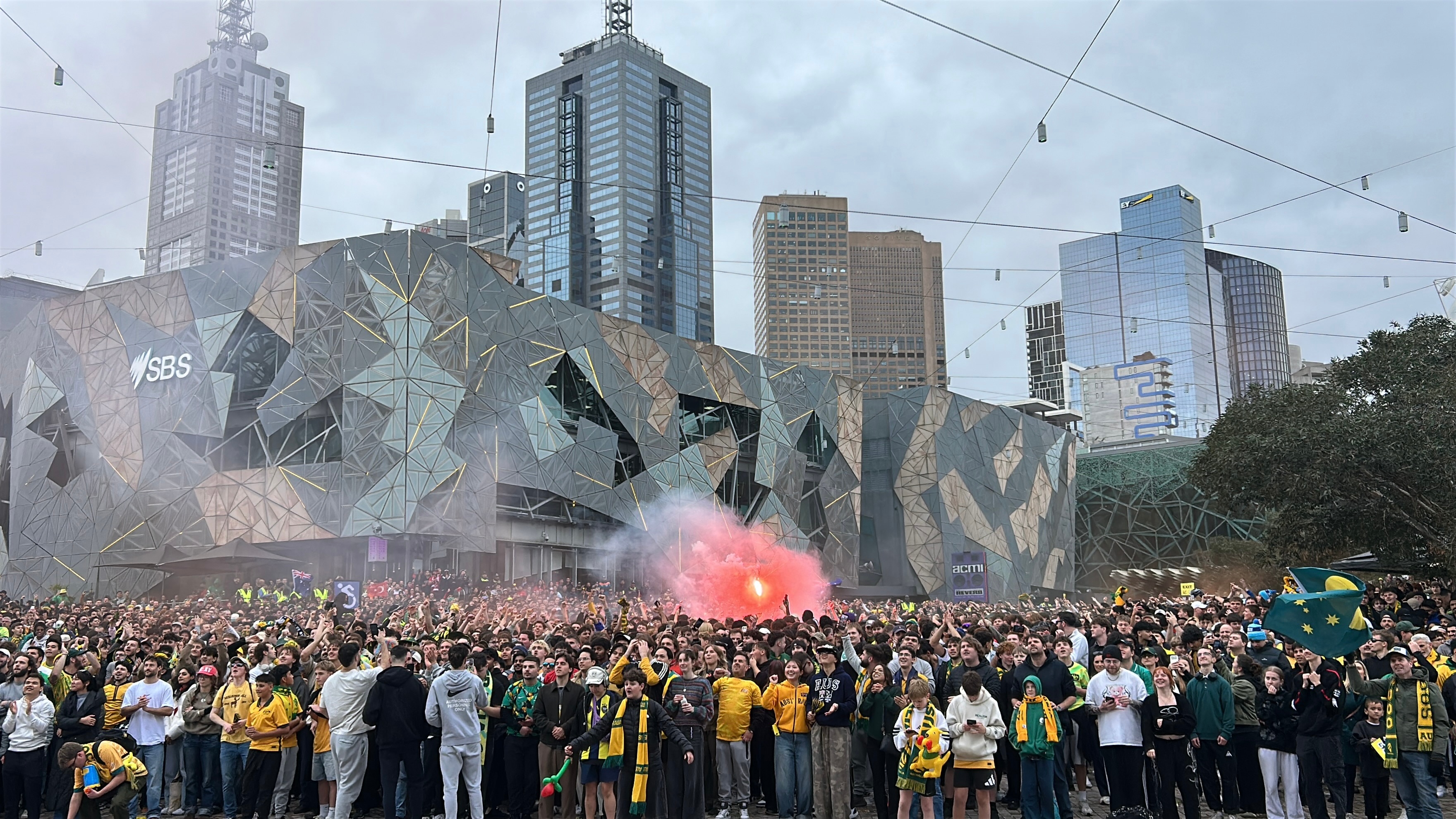 A flare is lit among a huge crowd at Federation Square