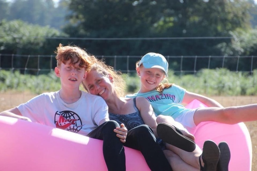 Mother Jennifer Guy smiles with in an outdoor photo with her kids.