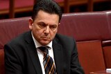 Senator Nick Xenophon sits alone with a pensive look on his face.