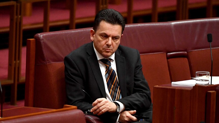 Senator Nick Xenophon sits alone with a pensive look on his face.