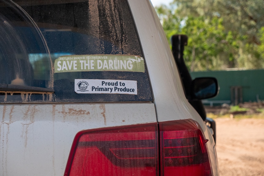 A dusty car shows two bumper stickers, one calling to save the Darling and another that reads 'proud to be a primary producer'