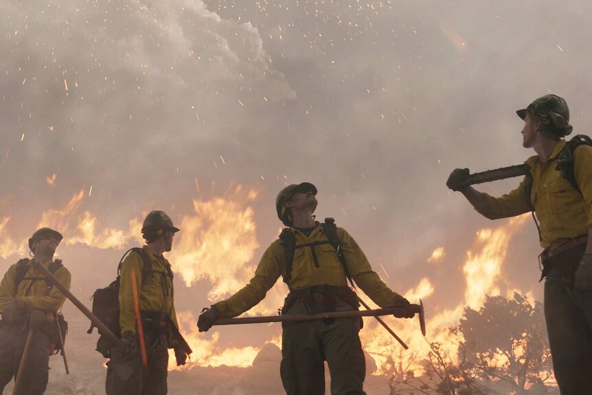 Still image from 2017 film Only The Brave of a crew of firefighters standing amongst scrubland on fire.