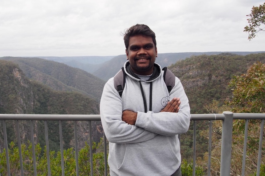 A man stands in front a railing overlooking mountains