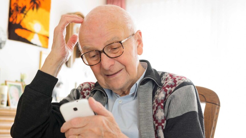An older man scratching his head looking at a smart phone