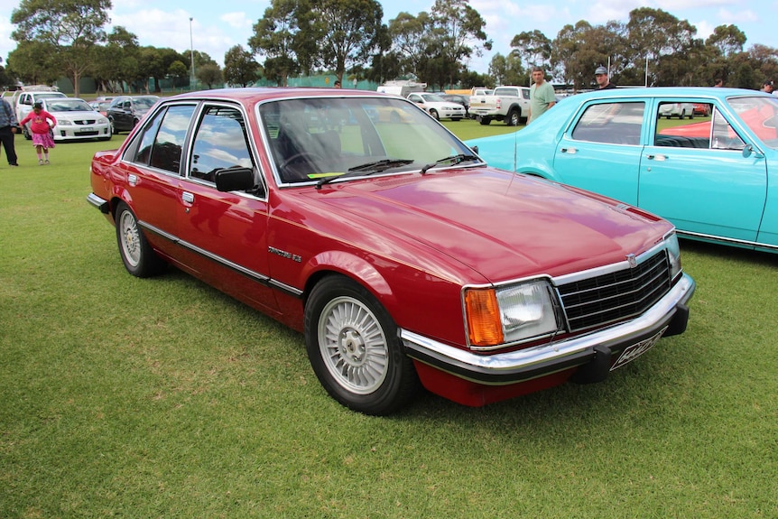 A red Holden Commodore SL/E parked at a car show.