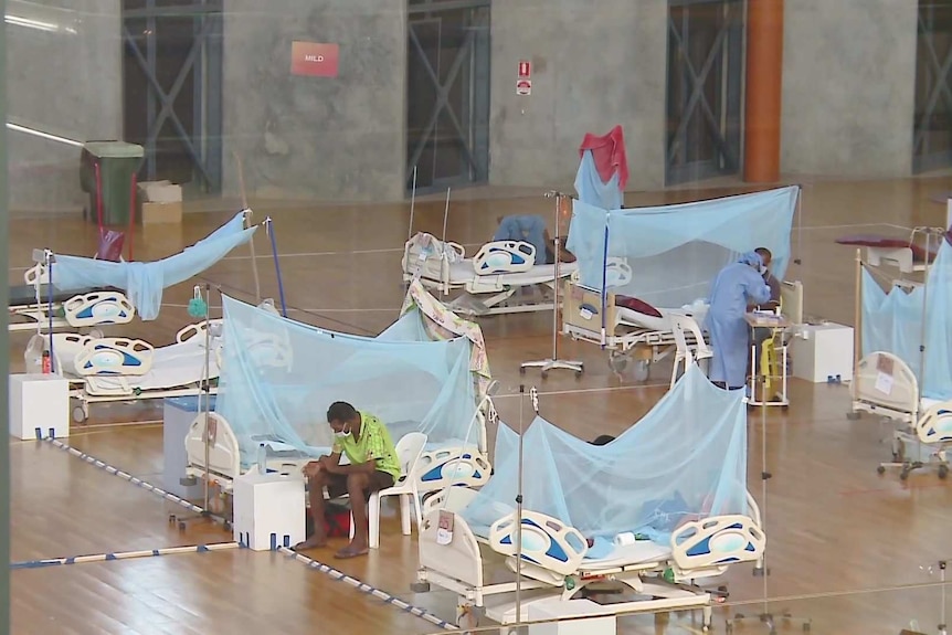 Hospital beds a few metres apart in an indoor sports arena.