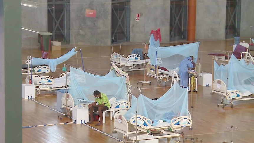 Hospital beds a few metres apart in an indoor sports arena.