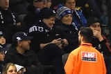 A security guard in an orange jacket watches the crowd at an AFL match