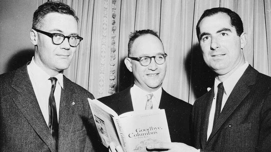Black and white photo of three men in suits, including a young Philip Roth all holding a copy of the book Goodbye Columbus