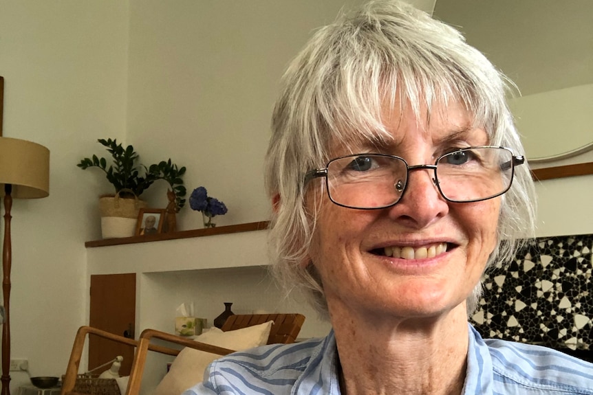 A selfie of a woman wearing glasses and a blue striped collared shirt. She has short white hair.