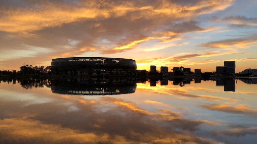 A wide shot looking over the Swan River showing Perth Stadium at dawn with clouds reflected on the water.
