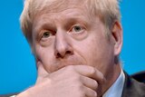 Conservative party leadership candidate Boris Johnson covers his mouth in front of blue background.