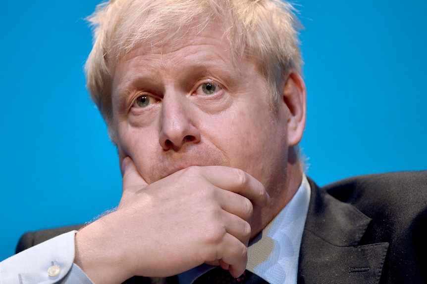 Conservative party leadership candidate Boris Johnson covers his mouth in front of blue background.