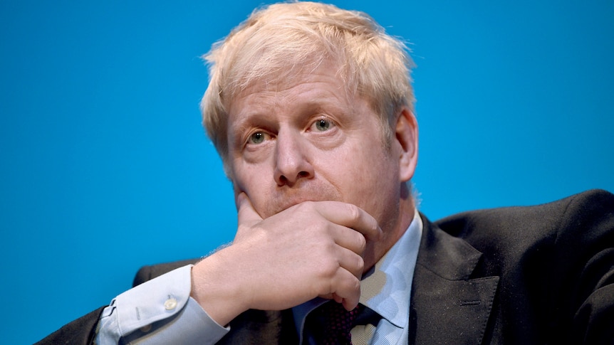 Conservative party leadership candidate Boris Johnson covers his mouth in front of blue background.