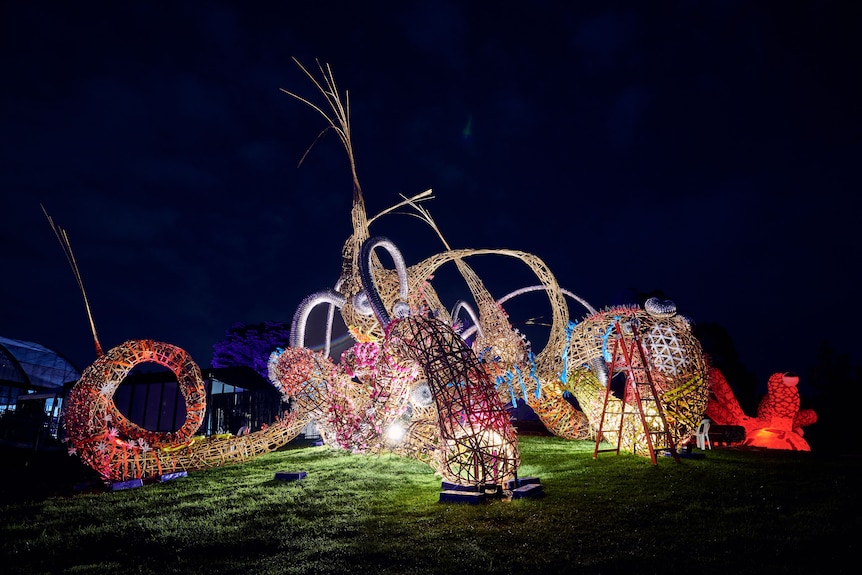 A large octopus-like sculpture made from bamboo is outside a live music venue, lit from below.