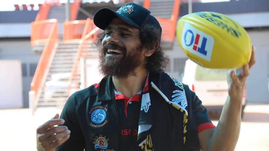 A bearded smiling man tossing a football around