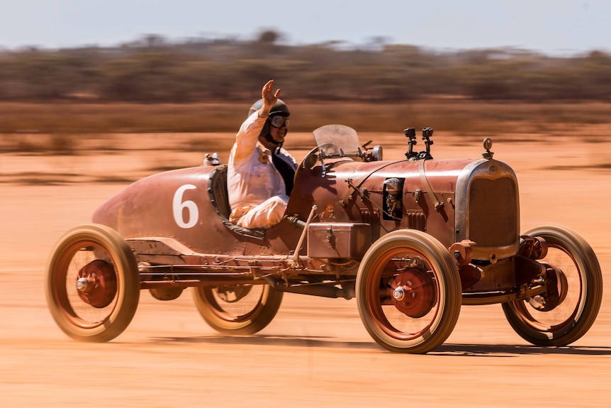 A man drives a vintage car on a race track.  
