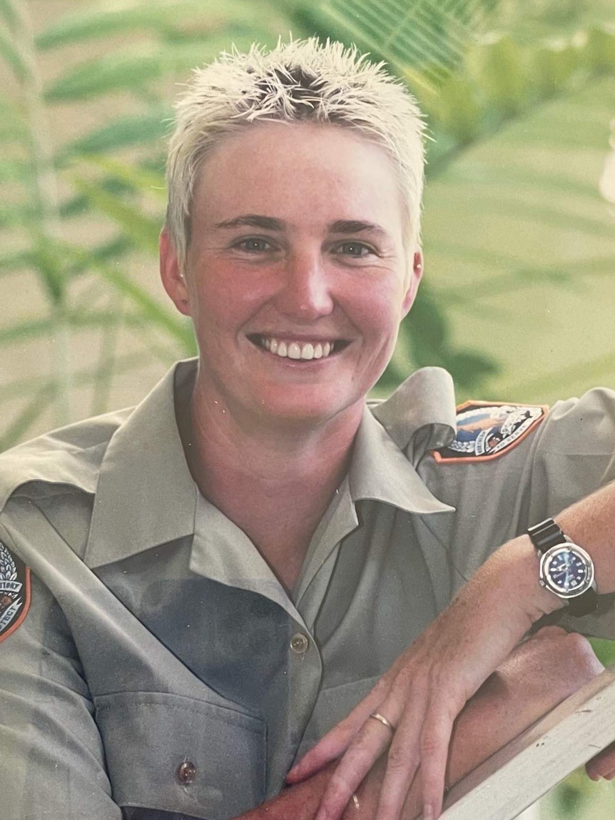 Woman with spiky blond hair wearing khaki police uniform smiling.