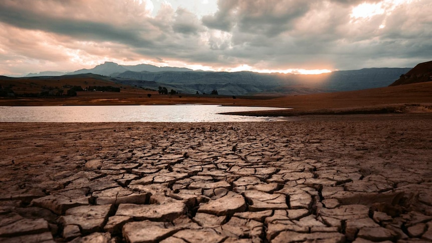 Cracked mud in the foreground leads to a diminishing supply of water with mountains in the background.