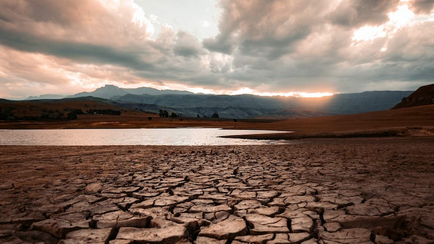 Cracked mud in the foreground leads to a diminishing supply of water with mountains in the background.