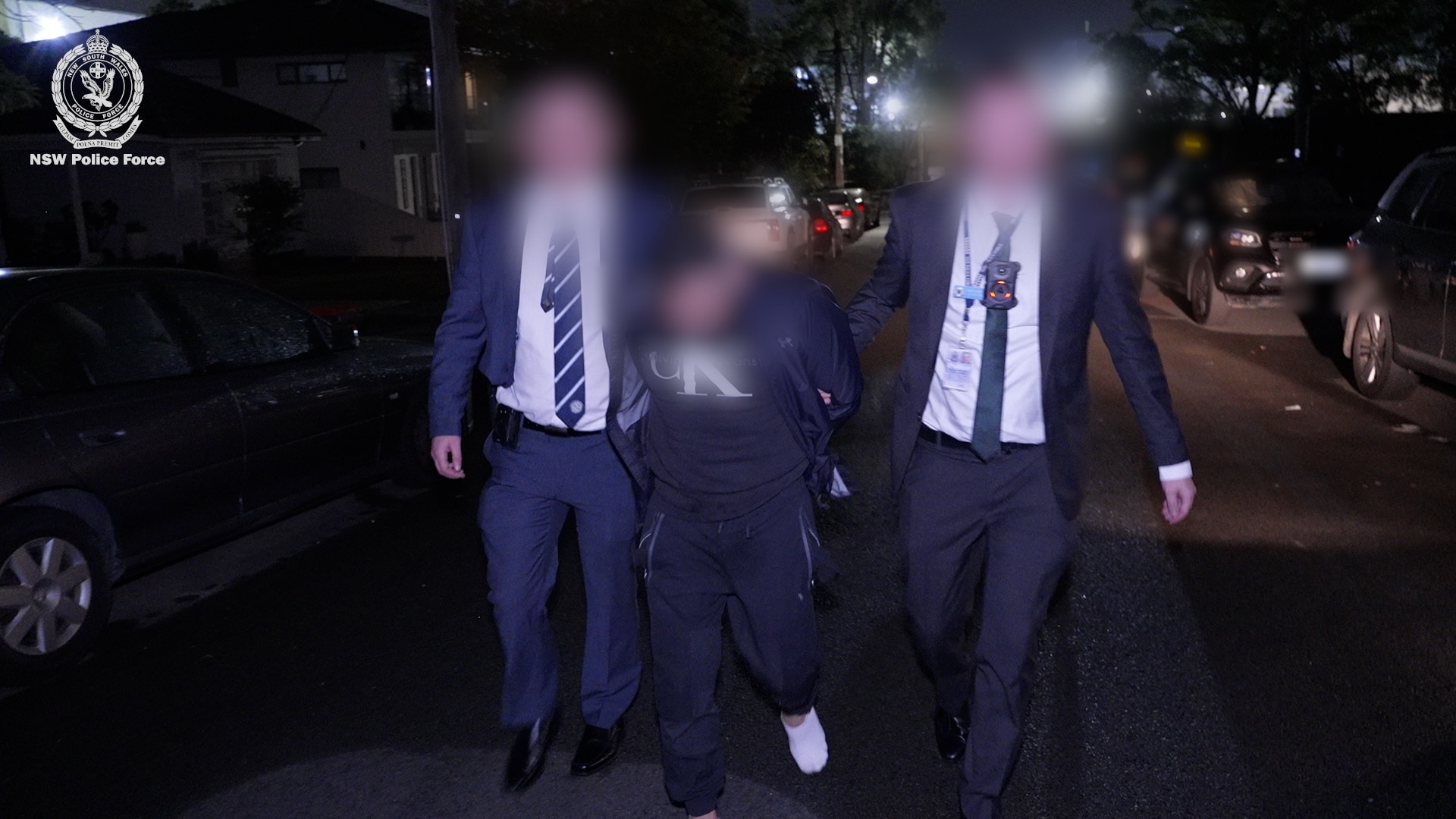 Man in black tracksuit, surrounded by police. Faces blurred