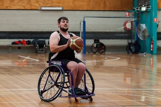 A man in a wheelchair, he is holding a basketball and is about to shoot it.