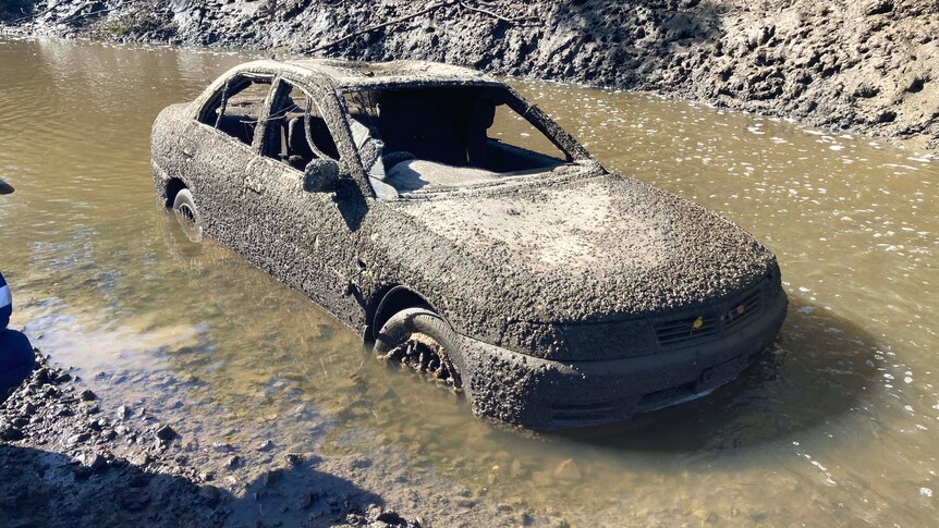 A car covered in barnacles partially submerged in muddy water 