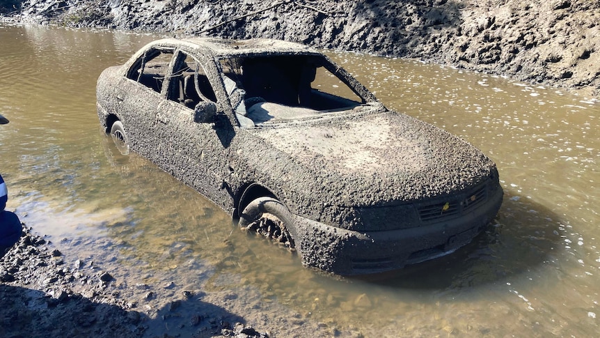 A car covered in barnacles partially submerged in muddy water 