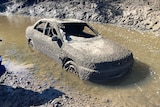 A car covered in barnacles partially submerged in muddy water 