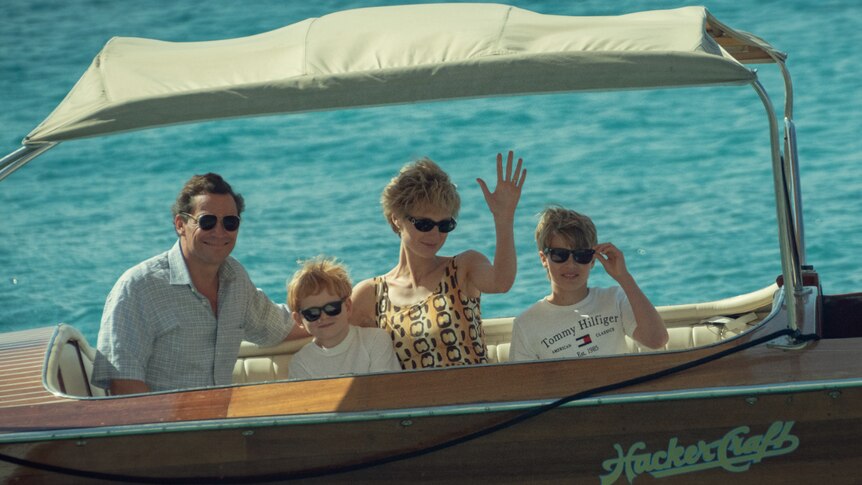 A family of four, resembling Prince Charles' young family, sits on a boat. 