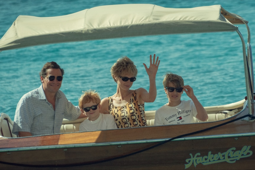 A family of four, resembling Prince Charles' young family, sits on a boat. 