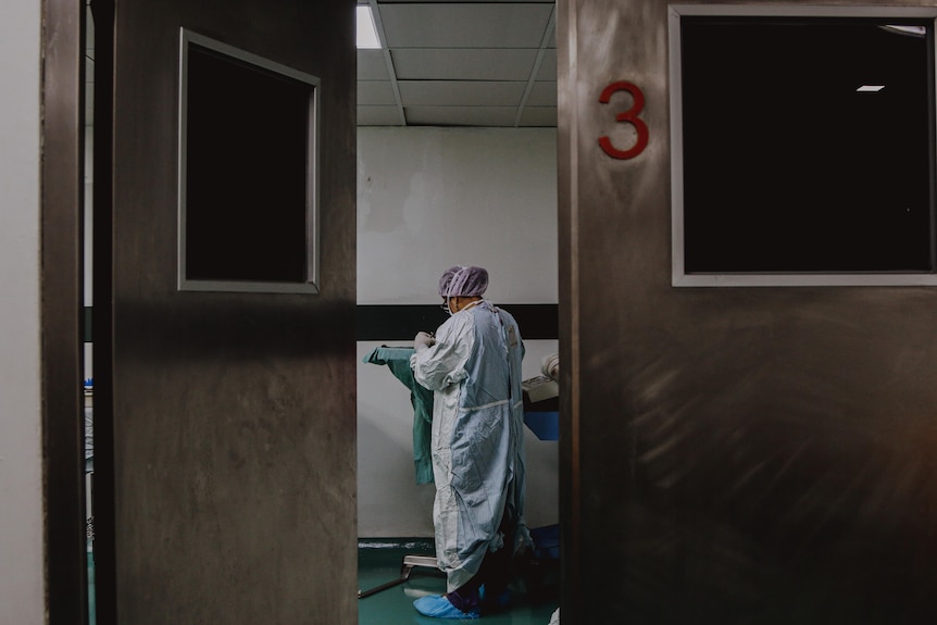 In the distance between two steel doors, a person in full doctor's scrubs looking down.