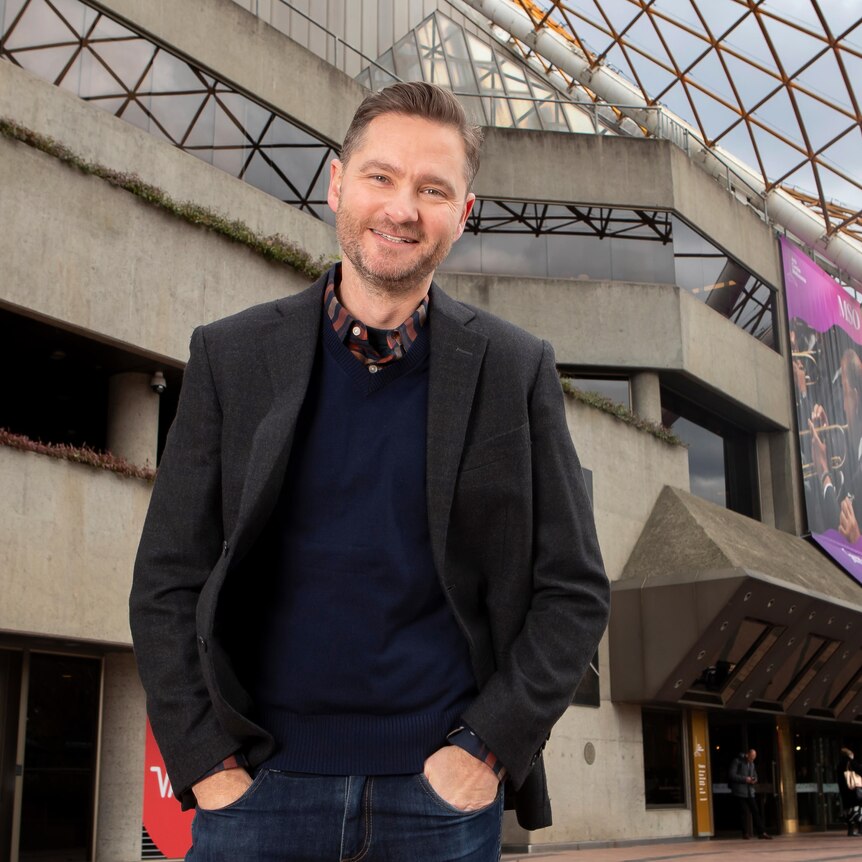 Charlie Pickering standing in front of the Arts Centre in Melbourne, with a little of the spire visible in the background.