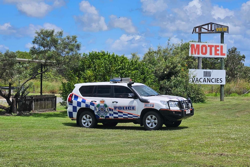 A police vehicle parked on grass with a broken motel sign visible behind