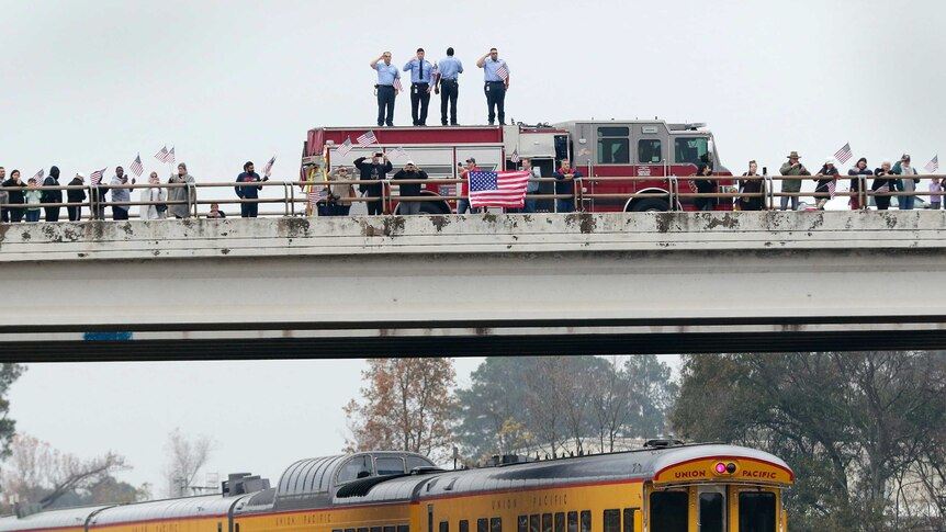 Firefighters stand on their truck and salute on an overpass as the train carrying the body of George HW Bush passes underneath.