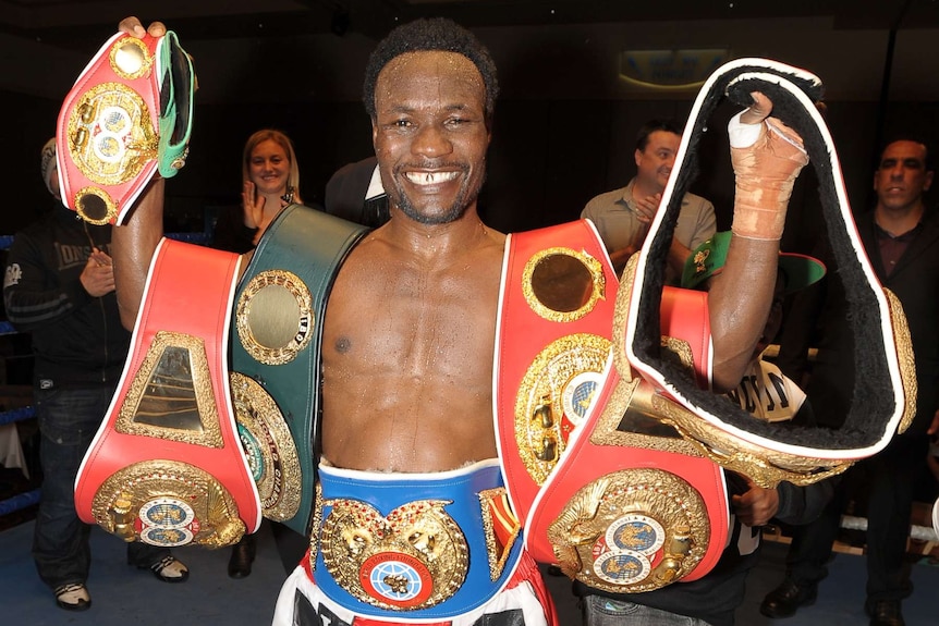 a man holding up several cummerbunds and belts and smiling