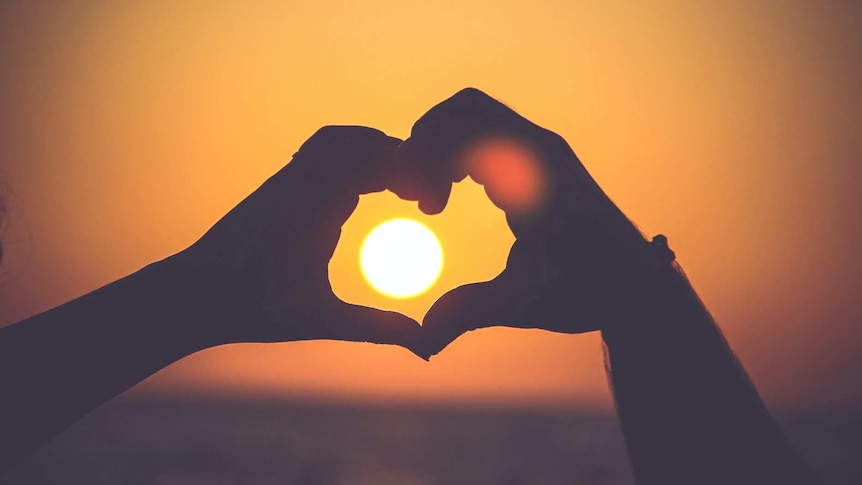 The hands of two people come together to form the shape of a love heart