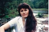 Portrait of a woman with long dark hair and white shirt sitting by a waterway