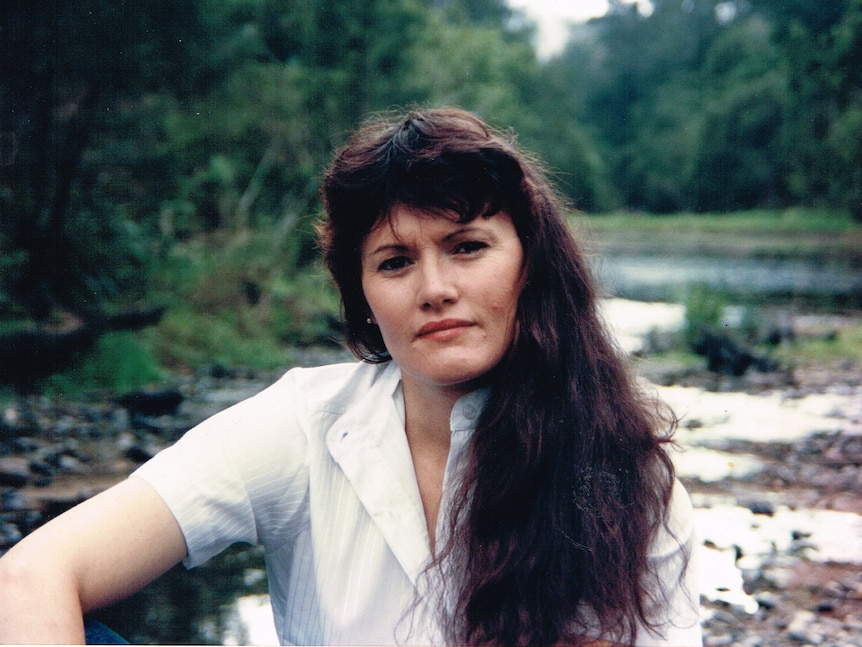 Portrait of a woman with long dark hair and white shirt sitting by a waterway