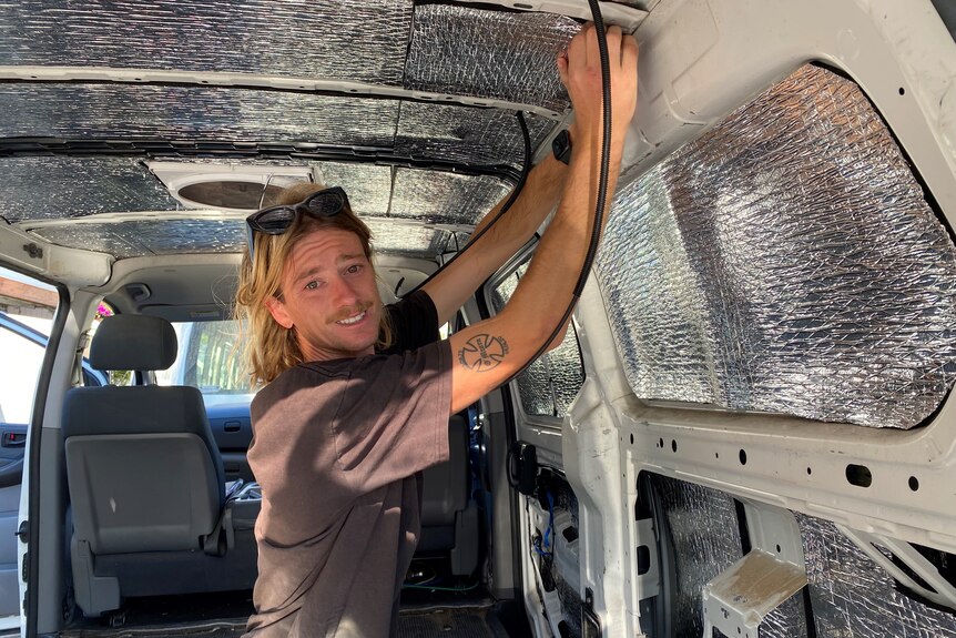 Man in rear of a van placing insulation on walls. 