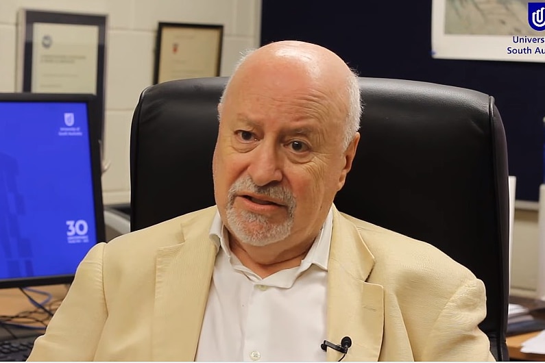 a man sitting at a desk talking into the camera