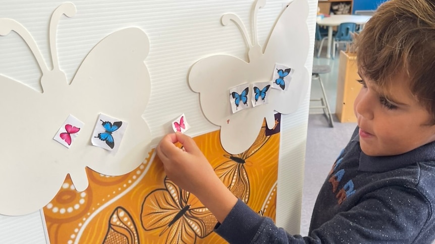 Child standing at a board putting on butterfly stickers 