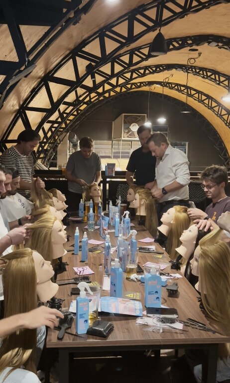Men gather around a table with head mannequins and style their hair.