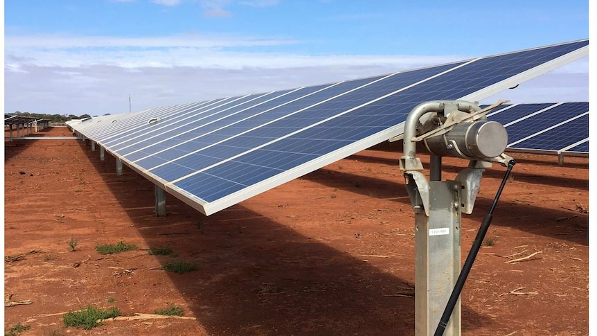 Long bank of chest high solar panels against blue sky on the red earth of the Sandfire copper mine near Meekatharra, WA